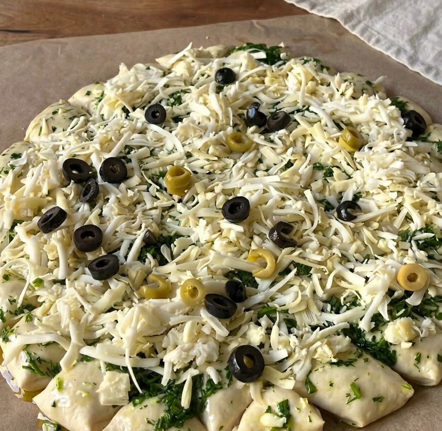 Vue de dessus dune pâte à pizza crue couverte de fromage râpé et garnie de nombreuses rondelles dolives noires et vertes.