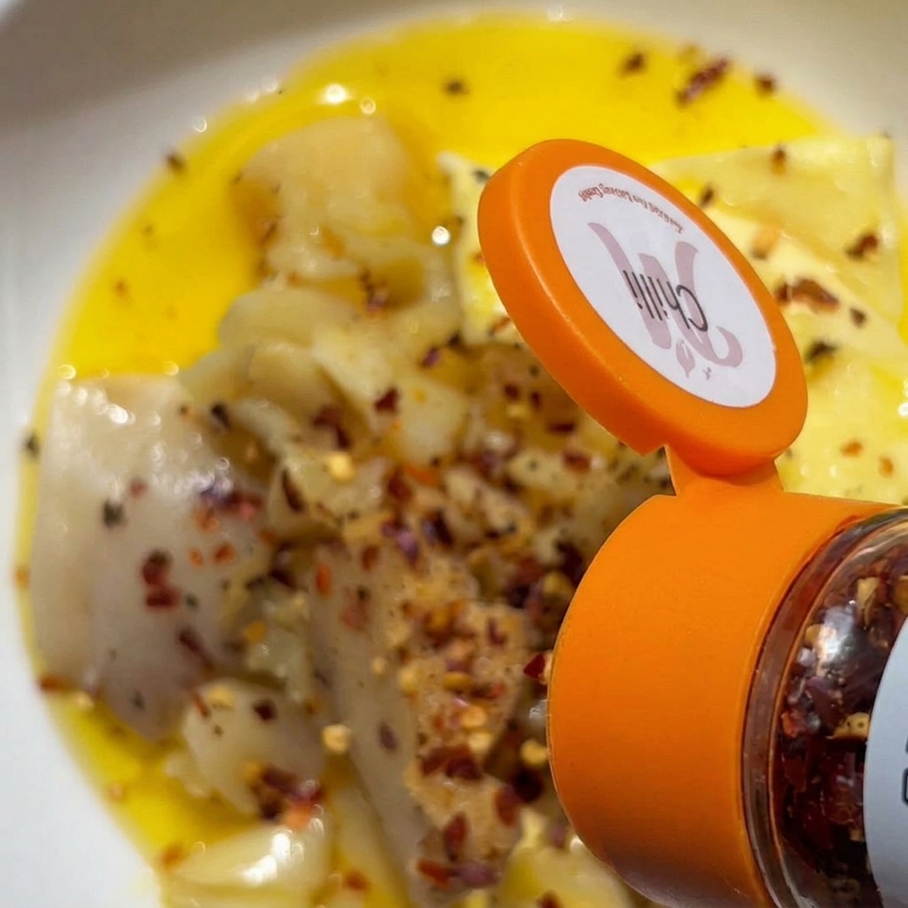 Flocons de piment versés depuis un flacon dépices à bouchon orange sur un bol dail écrasé et de beurre.