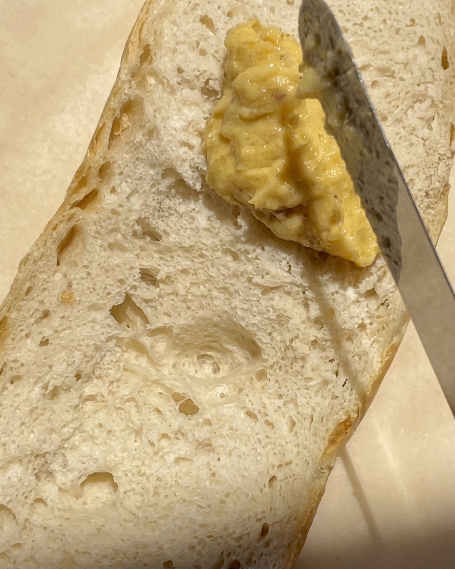 Gros plan dun couteau étalant un mélange épais et crémeux de beurre et dail rôti sur la surface alvéolée dune demi-baguette.