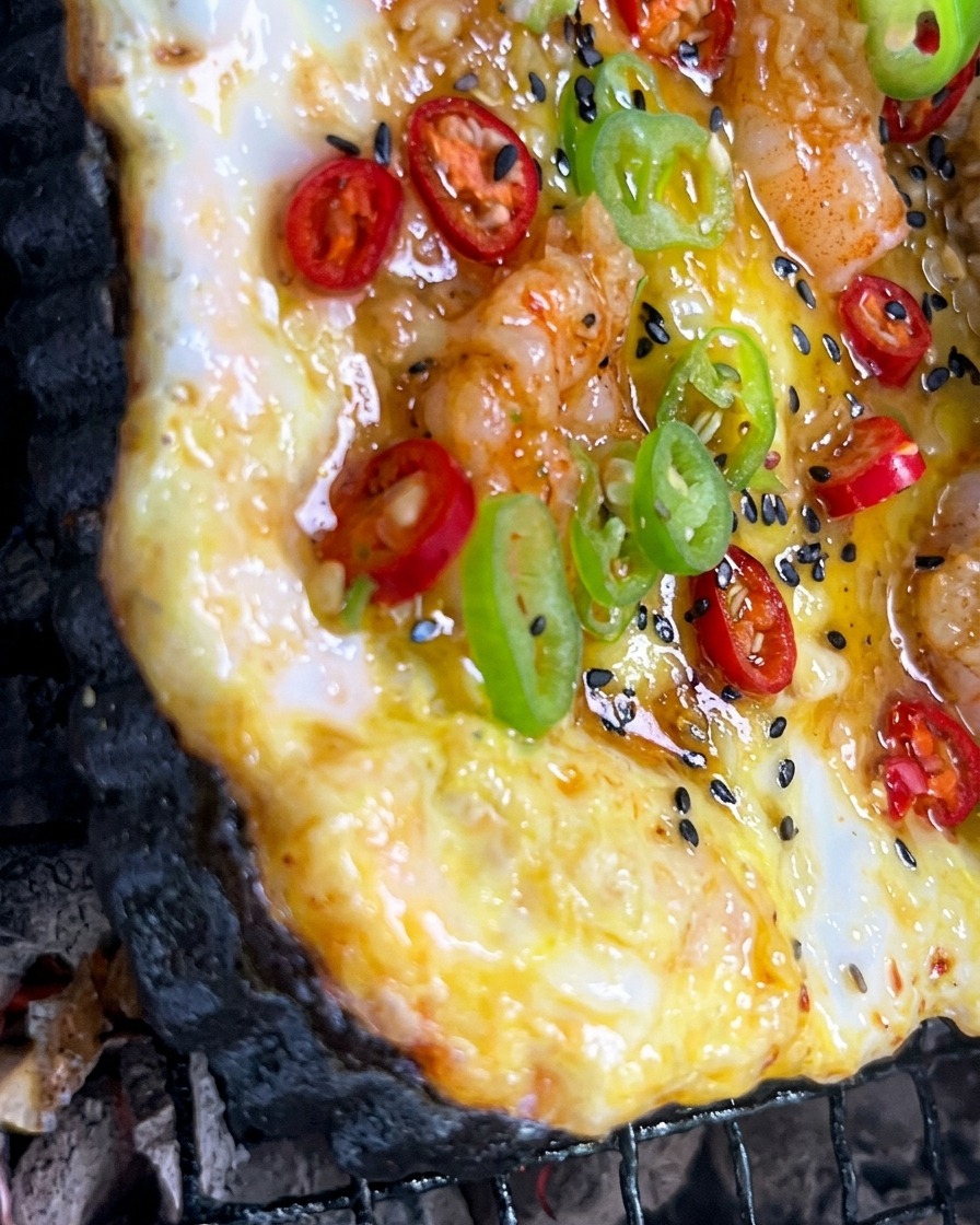 Une sauce à lail haché est étalée au pinceau sur une pizza colorée qui cuit au feu de bois.