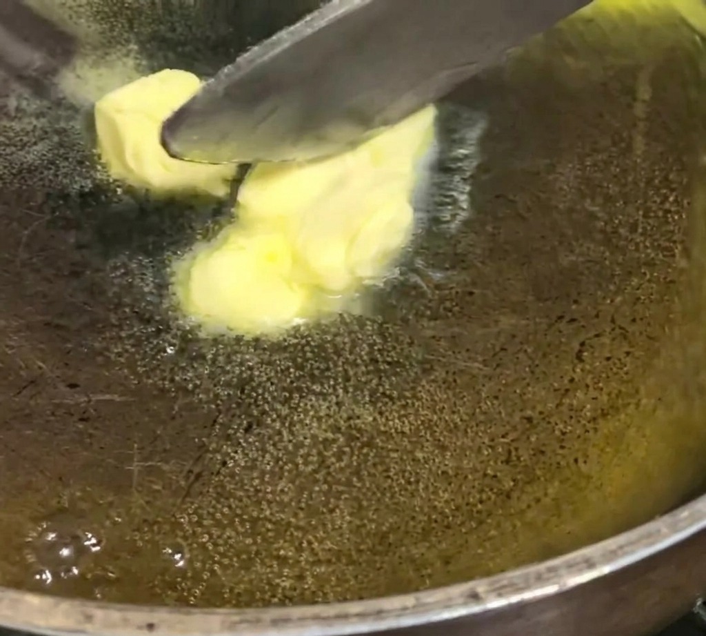 Cubes de beurre jaune fondant et crépitant doucement dans une poêle sur feu doux.