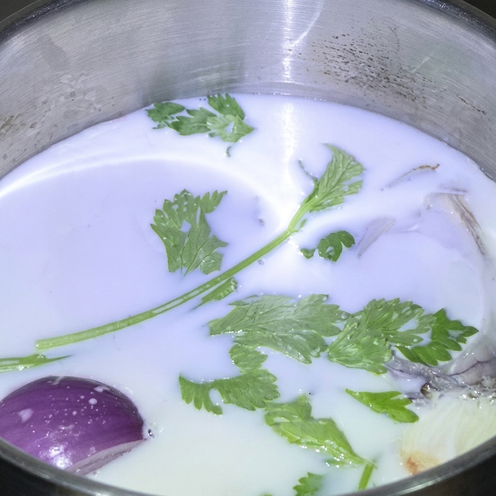 Herbes vertes fraîches et un quartier doignon rouge flottant dans du lait blanc au sein dune casserole en inox.