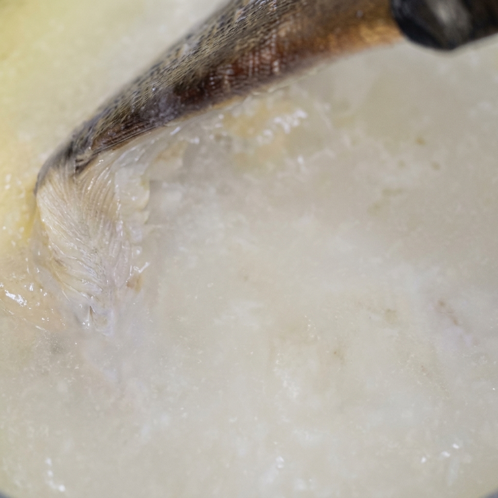 Un liquide pâle versé dans une poêle et mélangé à laide dun ustensile en bois, créant une base blanche et crémeuse.