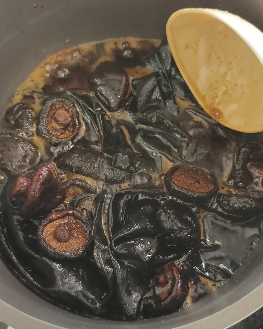 Gros plan sur des champignons noirs et de grands morceaux de kombu mijotant dans un liquide de soja brun foncé bouillonnant.
