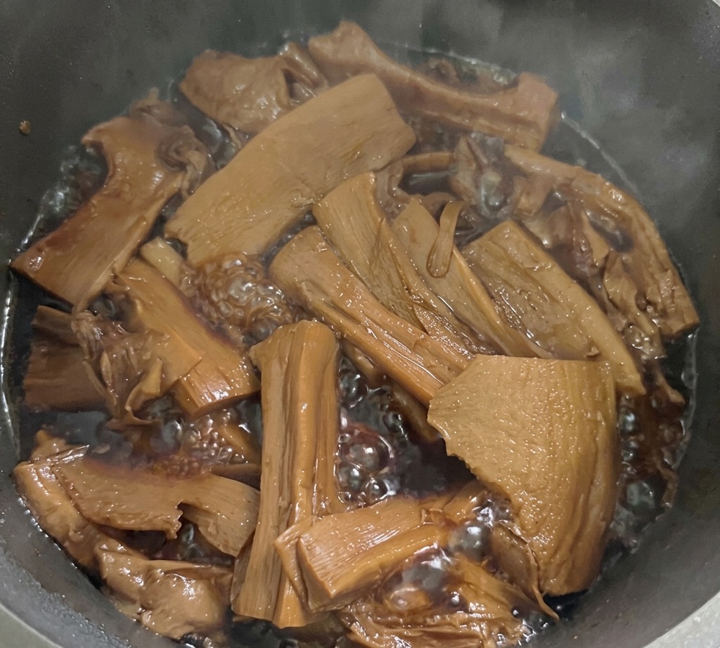 Tranches de pousses de bambou mijotant dans un liquide dassaisonnement brun foncé bouillonnant dans une casserole métallique sur la cuisinière.