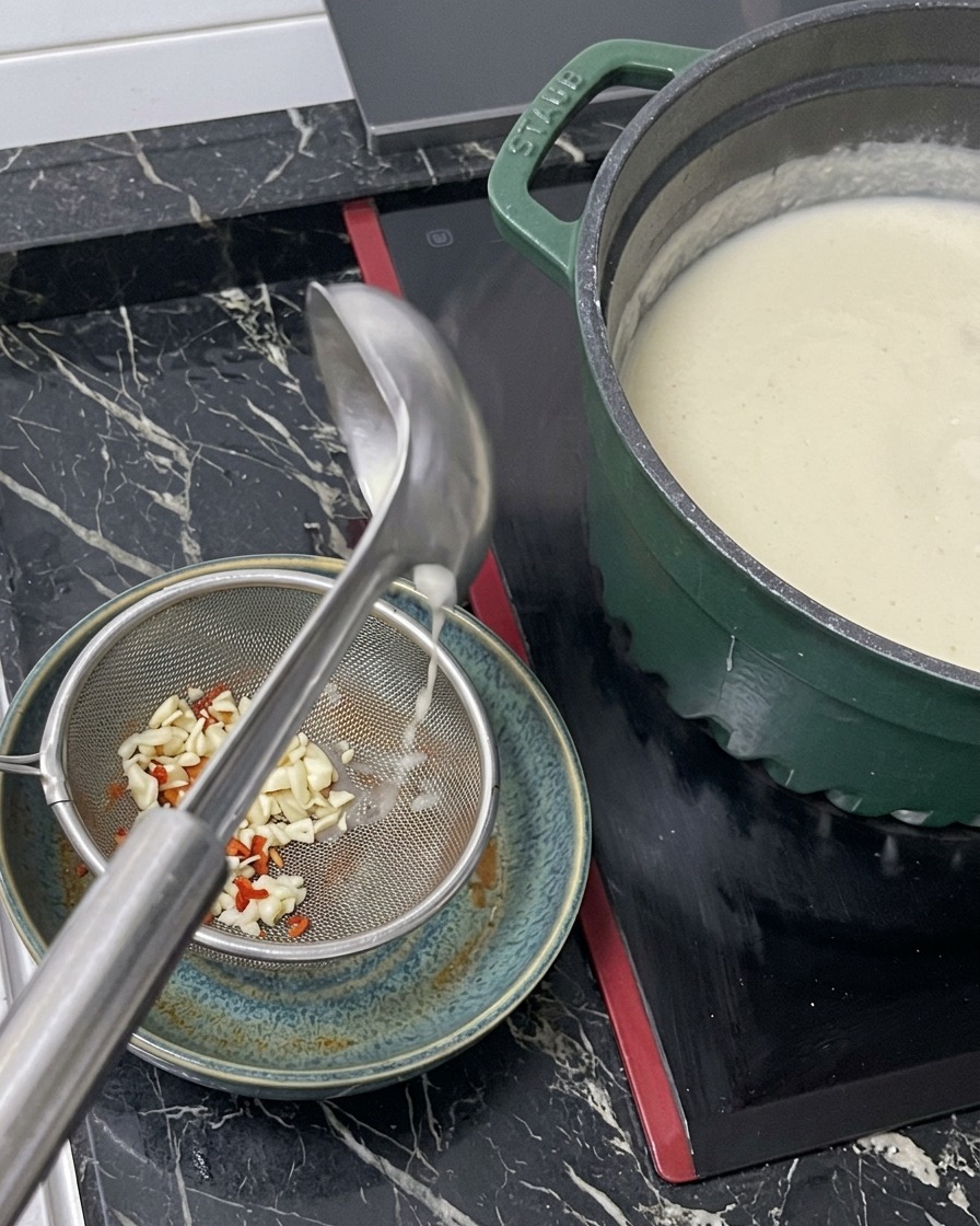 Bouillon blanc chaud versé dune louche à travers une passoire métallique dans un bol contenant la base dassaisonnement pour ramen.