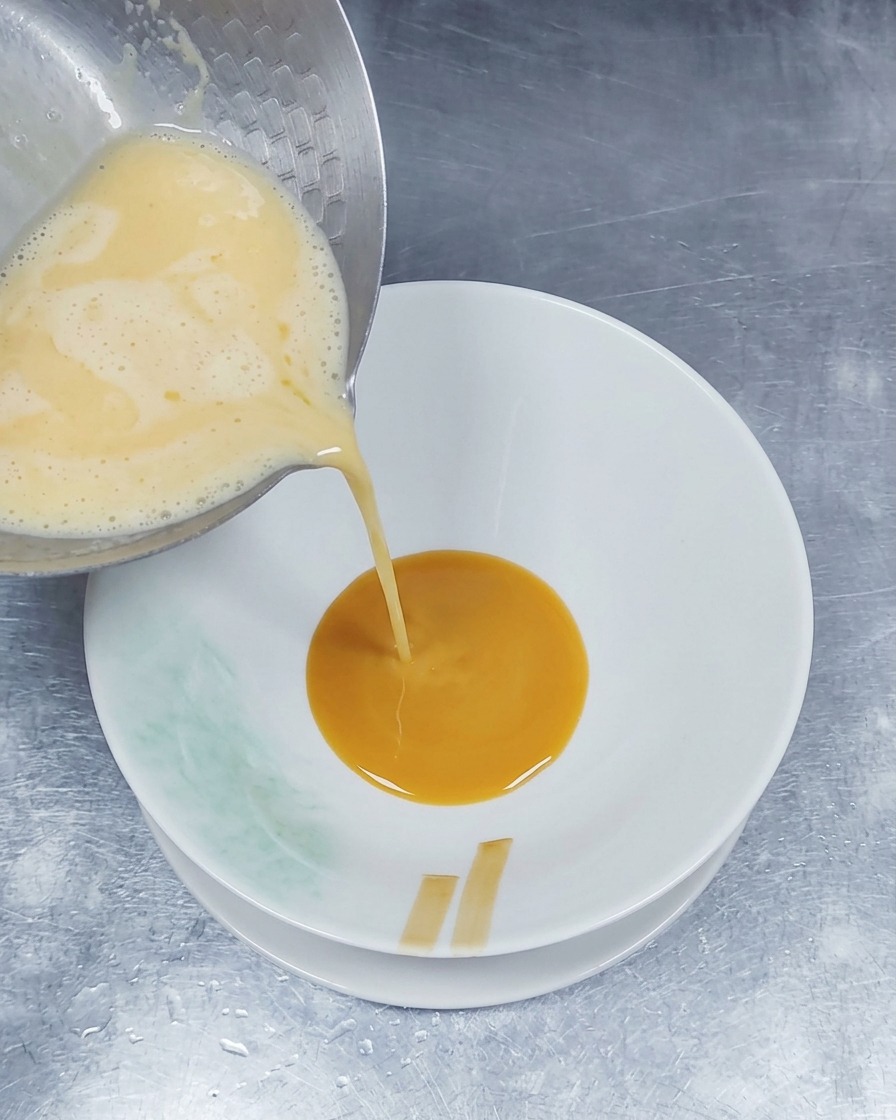 Un bouillon de porc chaud et mousseux versé depuis une casserole en métal dans un bol contenant déjà une couche de sauce dassaisonnement brune.