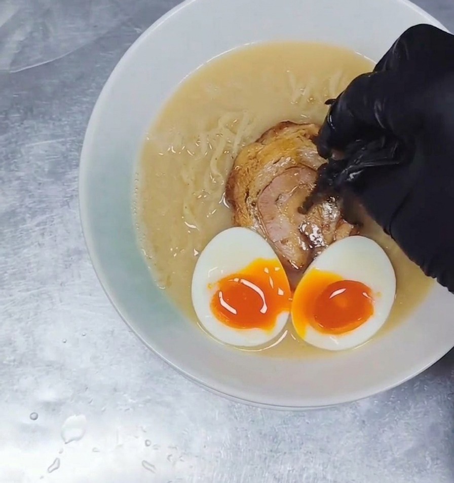 De fines lanières de champignons noirs ajoutées à un bol de ramen garni de bouillon, de nouilles, de porc et dœufs mollets.