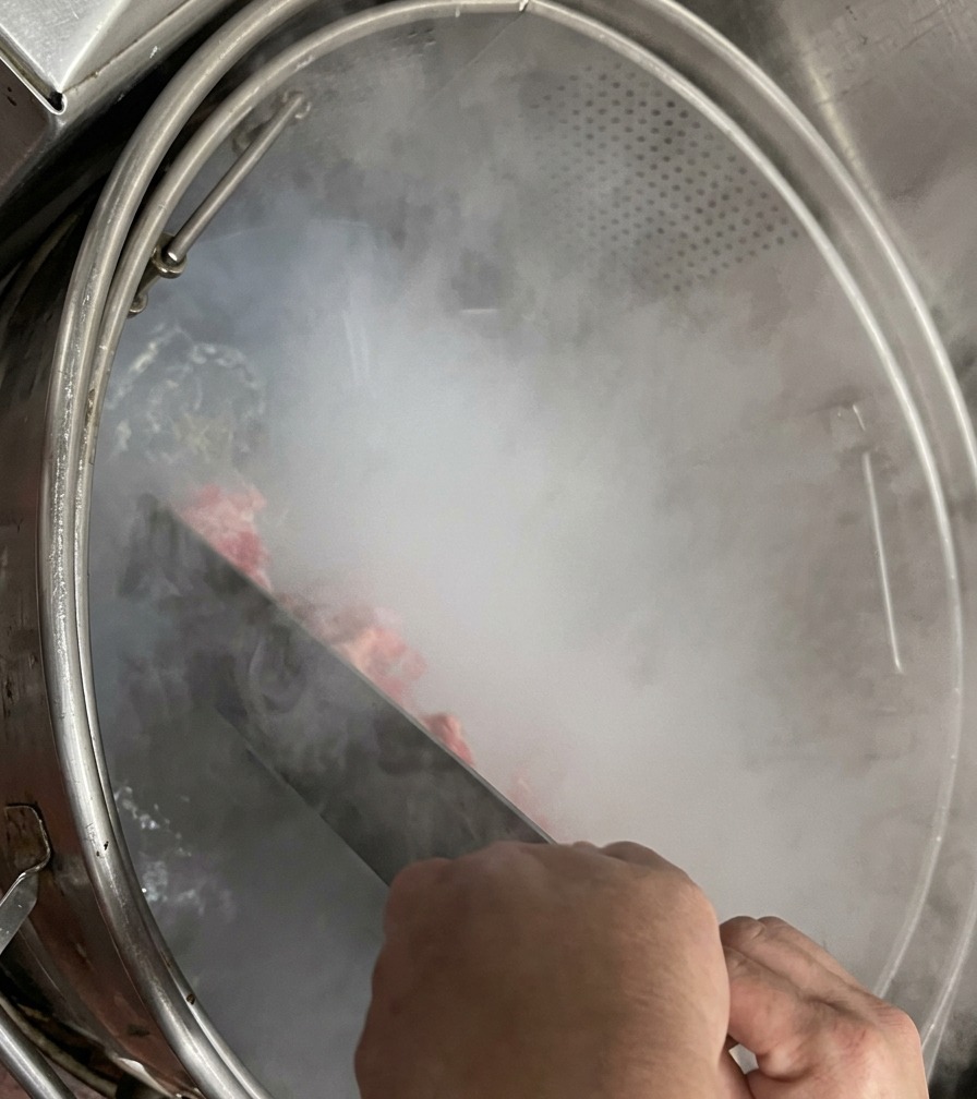 Des mains tenant une grande spatule en métal pour remuer les os de porc à lintérieur dune marmite bouillante fumante.