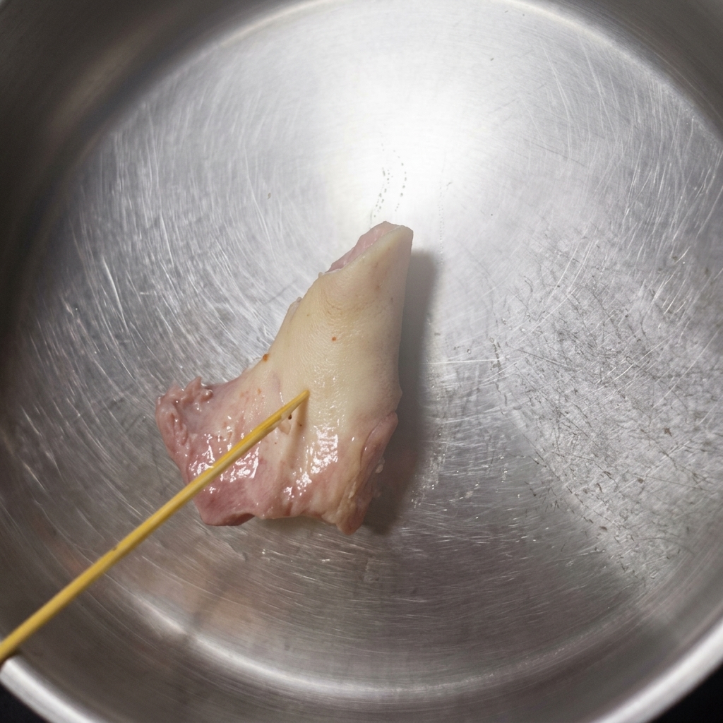 Une brochette en bois senfonçant dans un os de porc pâle et ramolli à lintérieur dun bol en acier inoxydable, montrant los qui commence à céder.