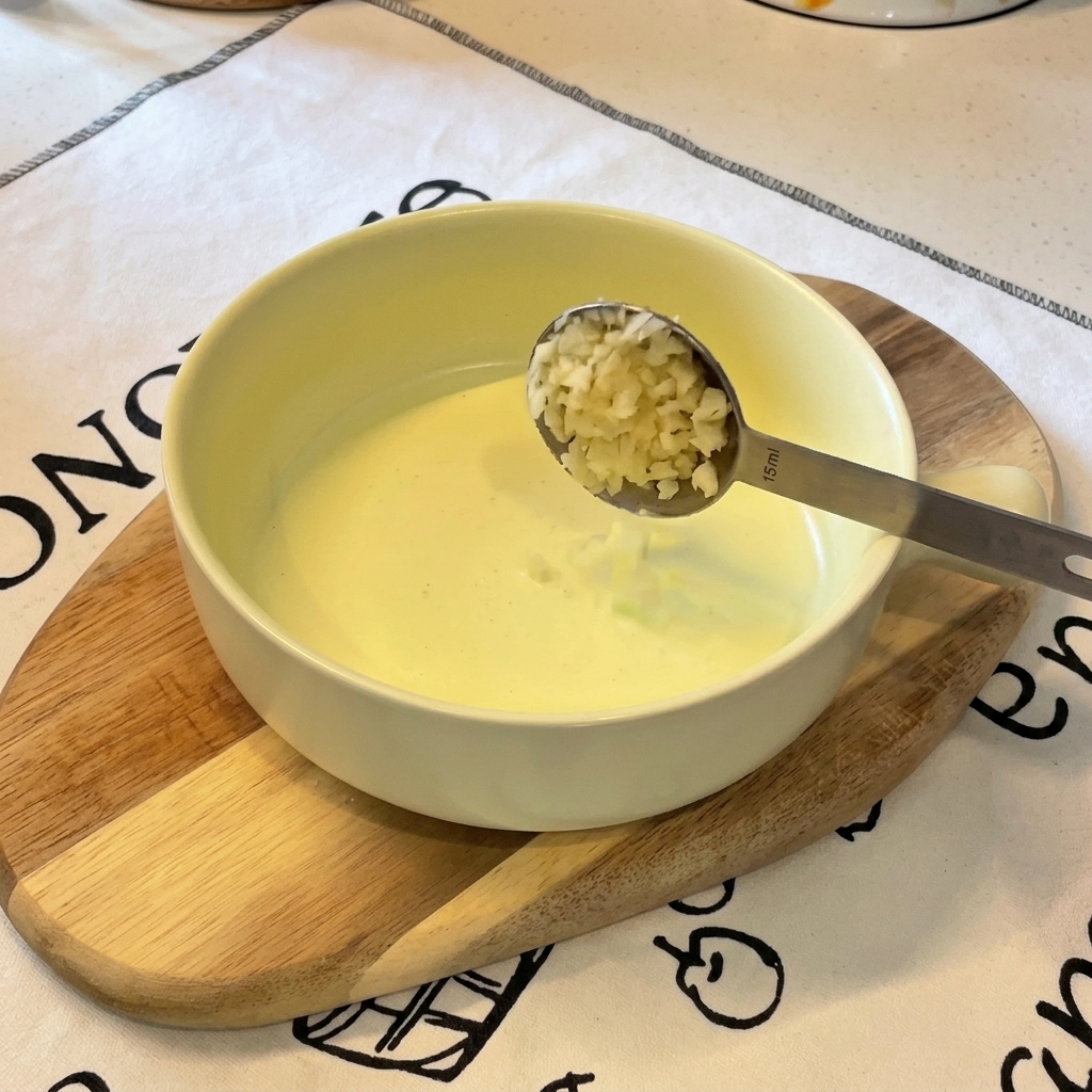 Une cuillère de cuisine verse de lail émincé dans un bol contenant déjà des oignons verts hachés.