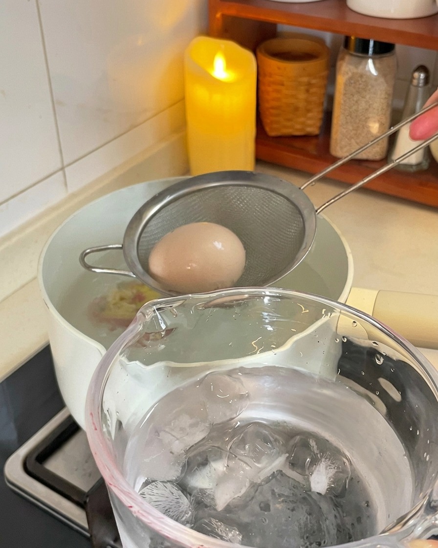 Une petite écumoire en métal sort un œuf bouilli dune casserole pour le plonger dans un récipient rempli deau et de glaçons.