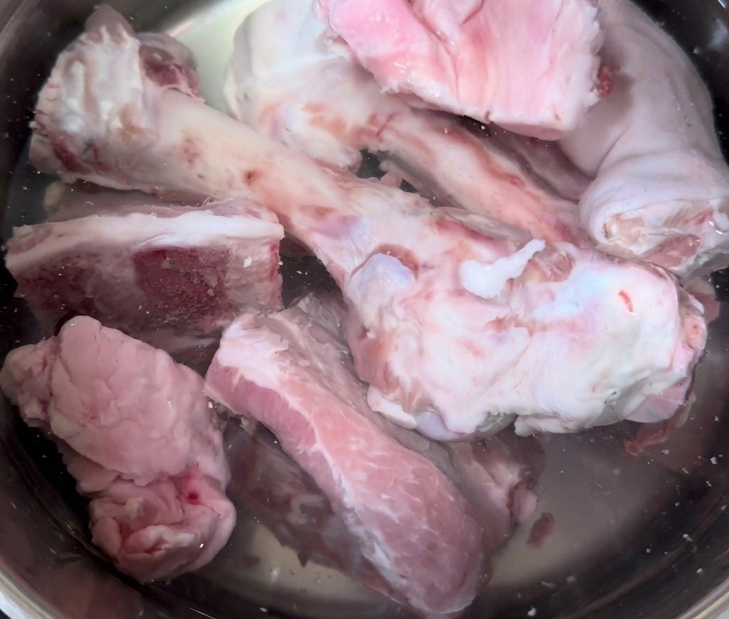 Os et pieds de porc crus plongés dans une grande marmite en acier inoxydable remplie deau froide.