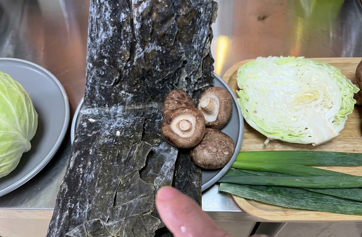 Sélection dingrédients frais comprenant du chou, de lalgue kombu et des champignons shiitake disposés sur un plan de travail.