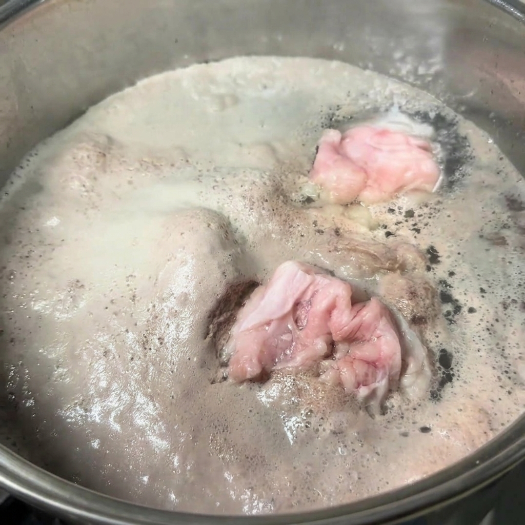 Marmite en acier inoxydable remplie deau bouillante et dos de porc, avec une épaisse couche décume grise à la surface.