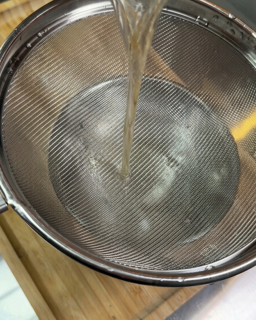Un filet de liquide brun foncé versé à travers une passoire métallique dans un bol en dessous.