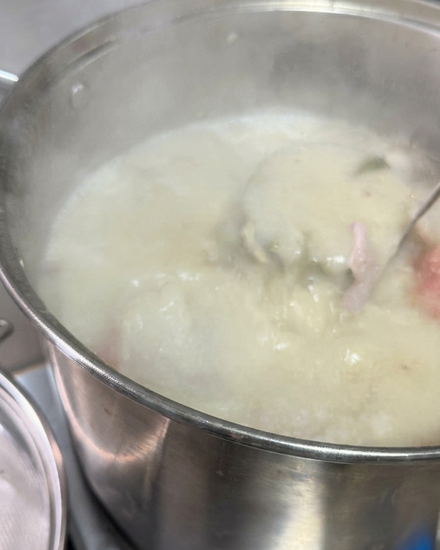 Bouillon de porc blanc laiteux versé à travers un tamis métallique dans une casserole contenant une sauce sombre et du saindoux.