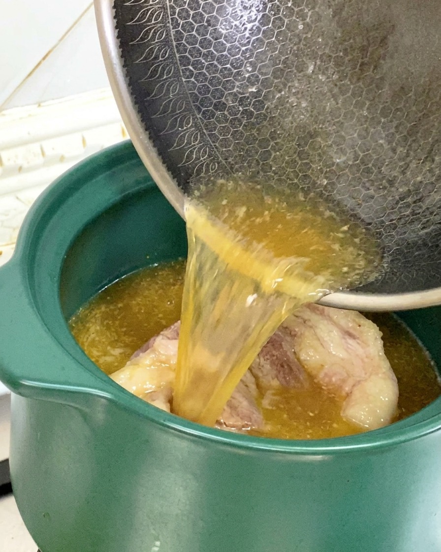 Versement du jus de cuisson et de lhuile du wok dans une marmite en terre verte contenant les os de porc.