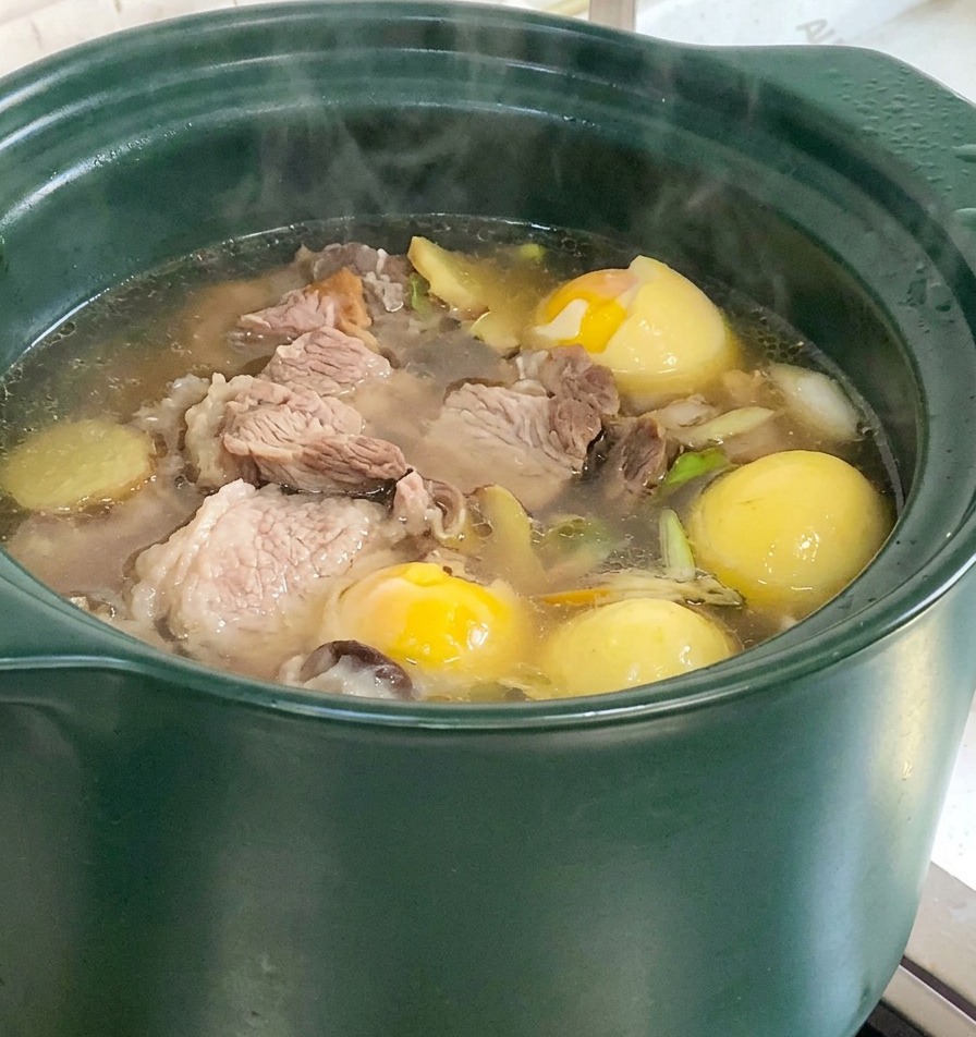 Soupe aux os de porc bouillonnante avec morceaux de maïs et digname visibles dans la marmite sur le feu.