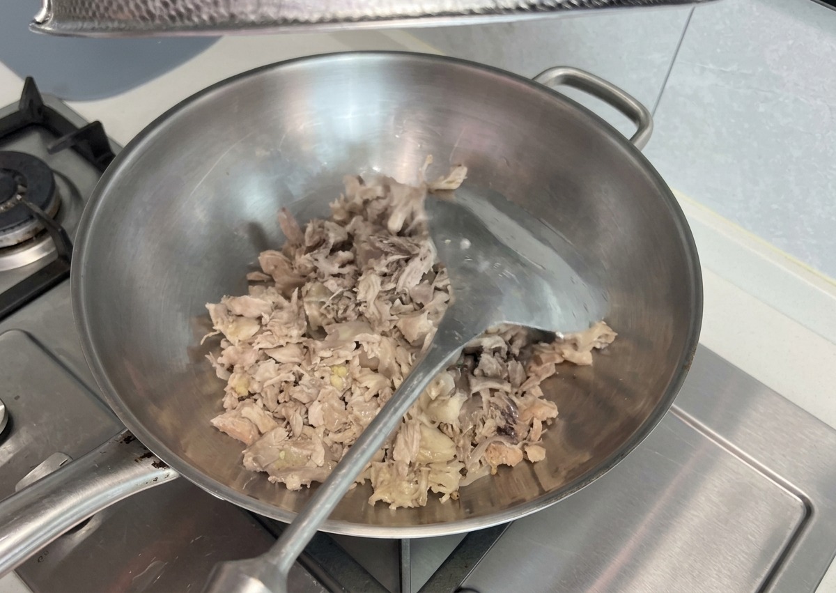 Restes de viande cuite effilochée, sautés et écrasés avec une spatule en métal dans un grand wok en acier inoxydable sur la cuisinière.