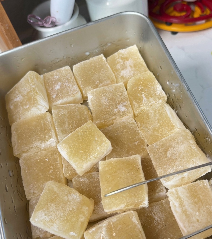 Un plateau en métal rempli de cubes de gelée de bouillon translucide jaune, découpés avec un ustensile en métal.