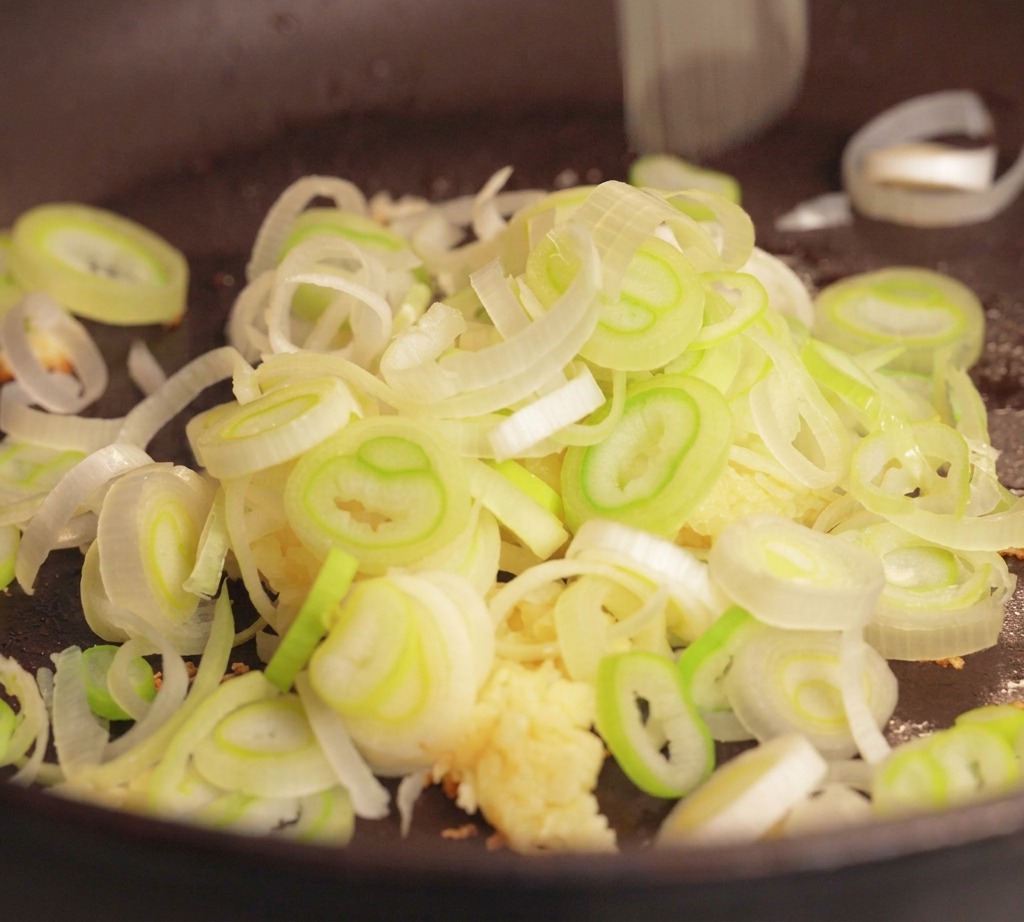 Porc haché cru, ail émincé et oignons verts tranchés prêts à être cuits dans une poêle sombre.
