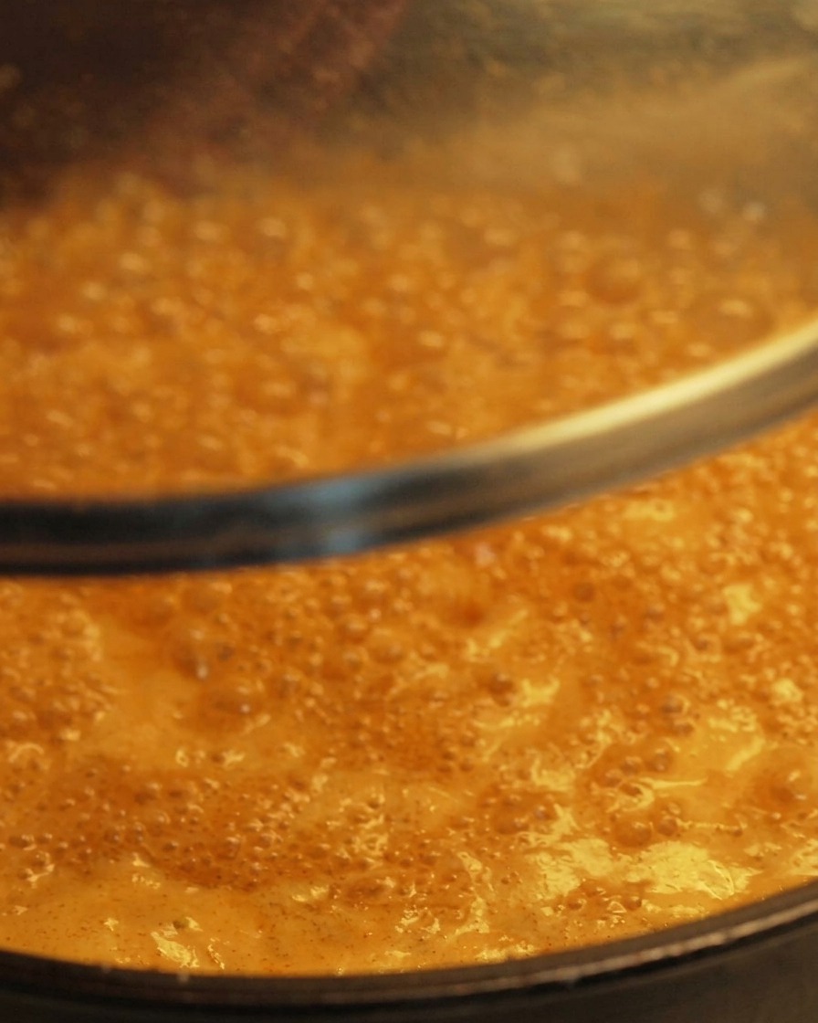 Un couvercle en verre transparent est posé sur une poêle contenant une sauce frémissante de couleur orange.