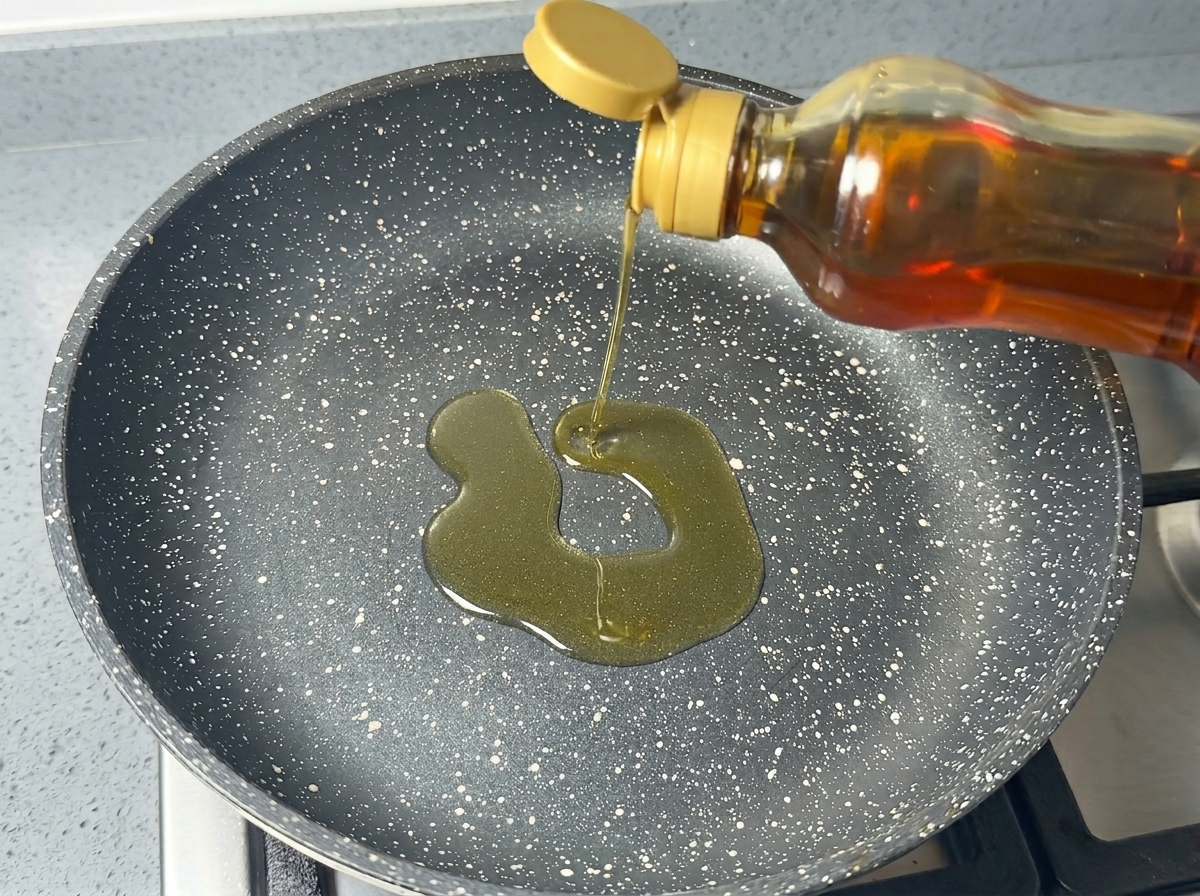 De lhuile de cuisson versée depuis une bouteille dans une poêle antiadhésive sombre et mouchetée.