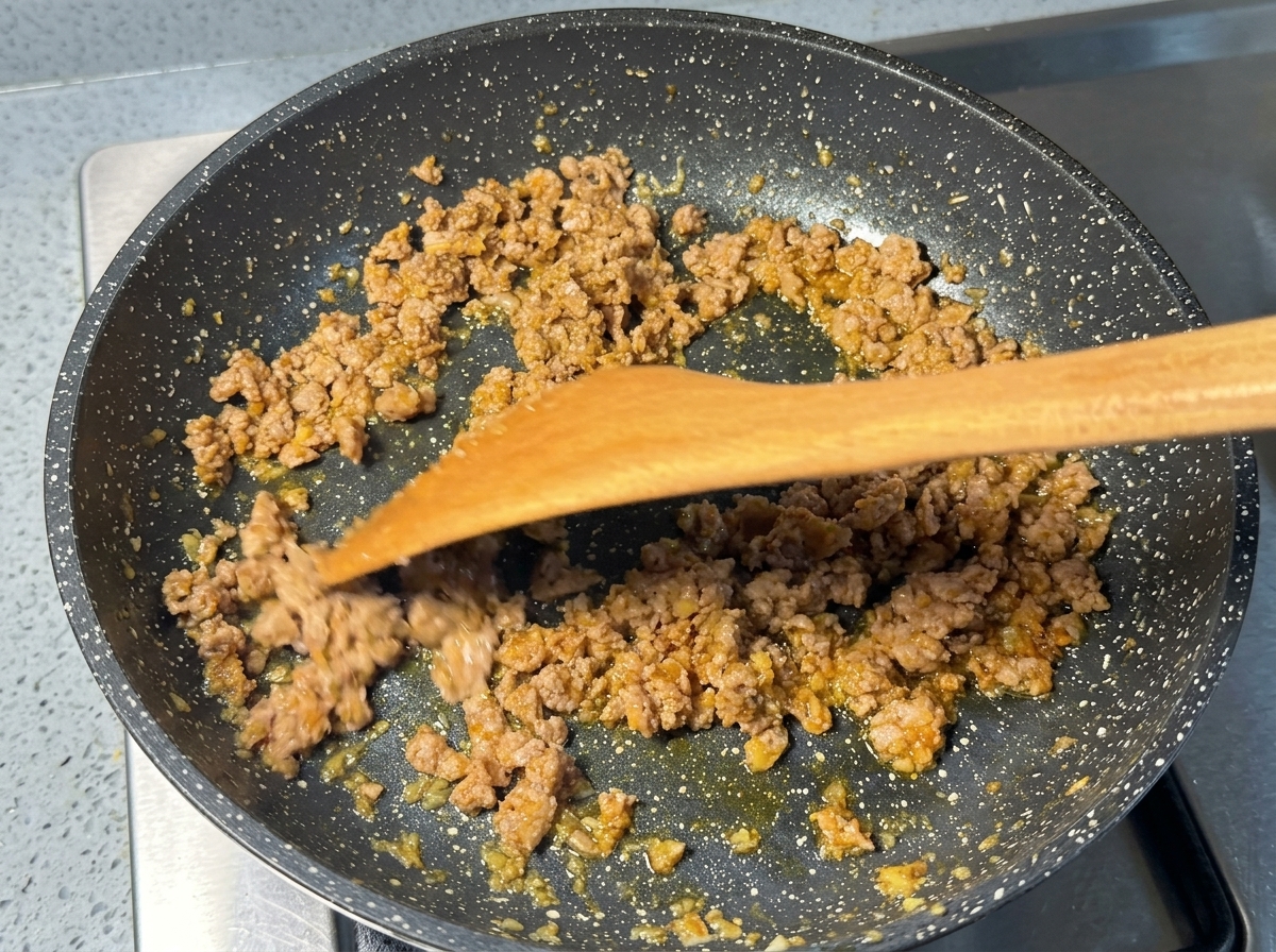 Du porc haché doré revenu dans une poêle mouchetée à laide dune spatule en bois.