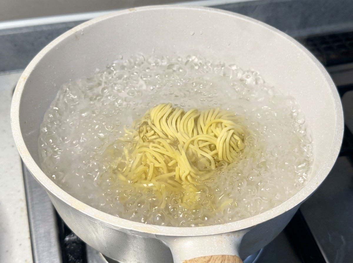 Un nid de nouilles ramen jaunes et fraîches bouillant à gros bouillons dans une casserole blanche remplie deau chaude.
