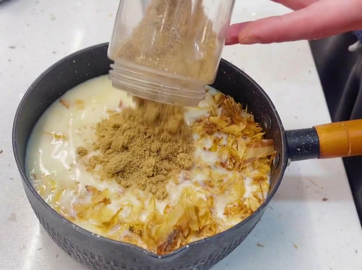 Le bol dun mixeur en plastique versant des graines de sésame finement moulues dans une casserole remplie de liquide blanc, de thon et de bonite.