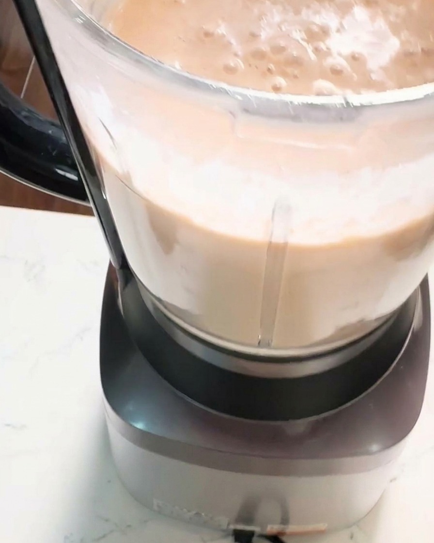 Gros plan sur un bol de mixeur contenant une épaisse pâte de crevettes rose orangé, lisse et crémeuse.
