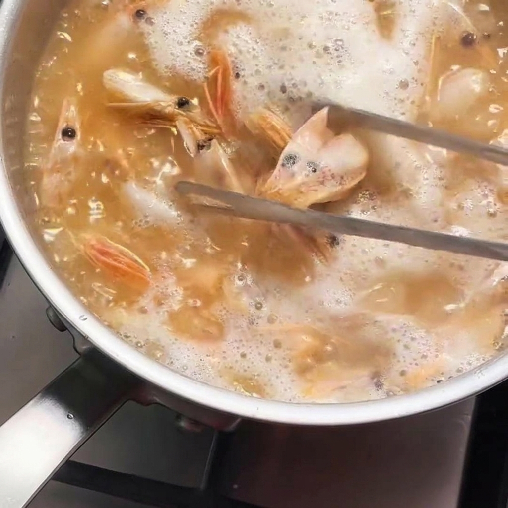 Des têtes de crevettes remuées avec une pince en métal dans une casserole dhuile chaude et frémissante prenant une couleur orange vif.