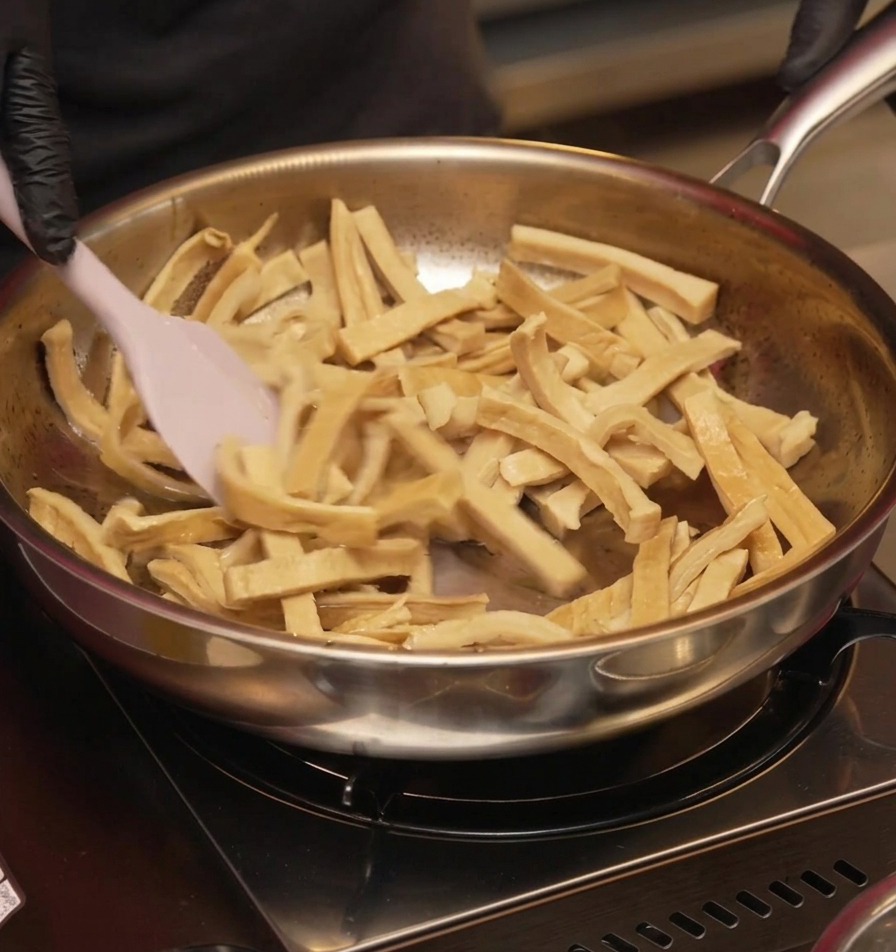 Des pousses de bambou émincées sautées dans une poêle à laide dune spatule en silicone rose jusquà ce quelles paraissent sèches et légèrement dorées.