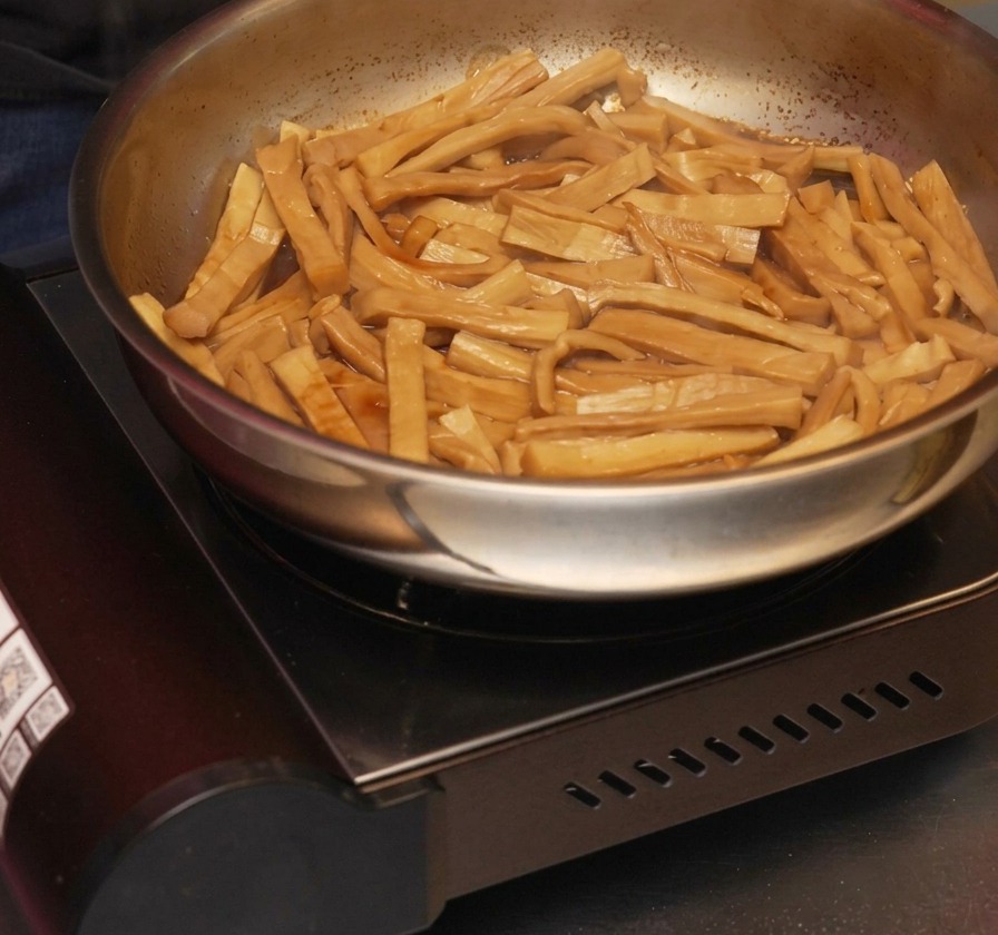 De lhuile de sésame versée en filet dans une poêle de pousses de bambou assaisonnées qui sautent dans une sauce réduite et foncée.