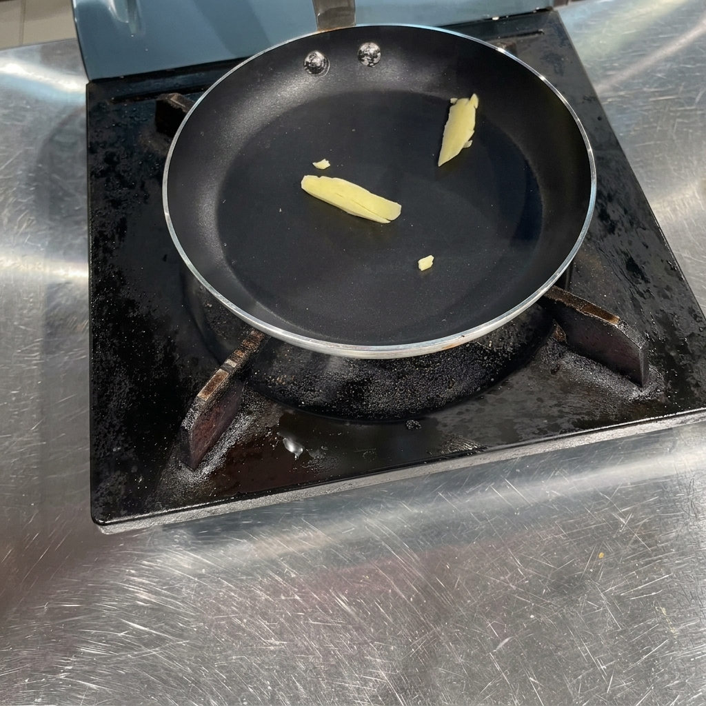 Un morceau de beurre jaune fondant dans une poêle noire à fond plat sur une plaque de cuisson.