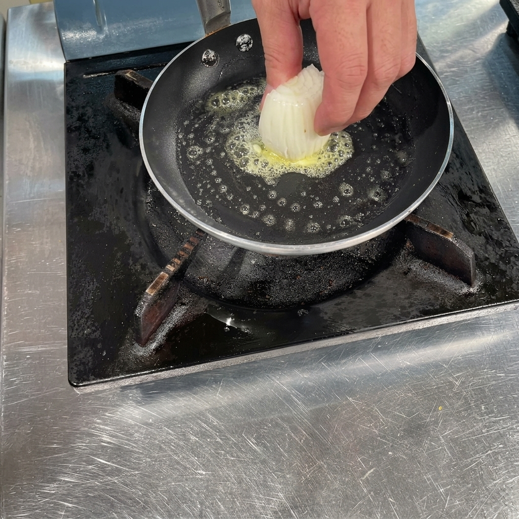 Une main déposant des morceaux doignons blancs émincés dans une poêle chaude avec du beurre fondu qui frémit.