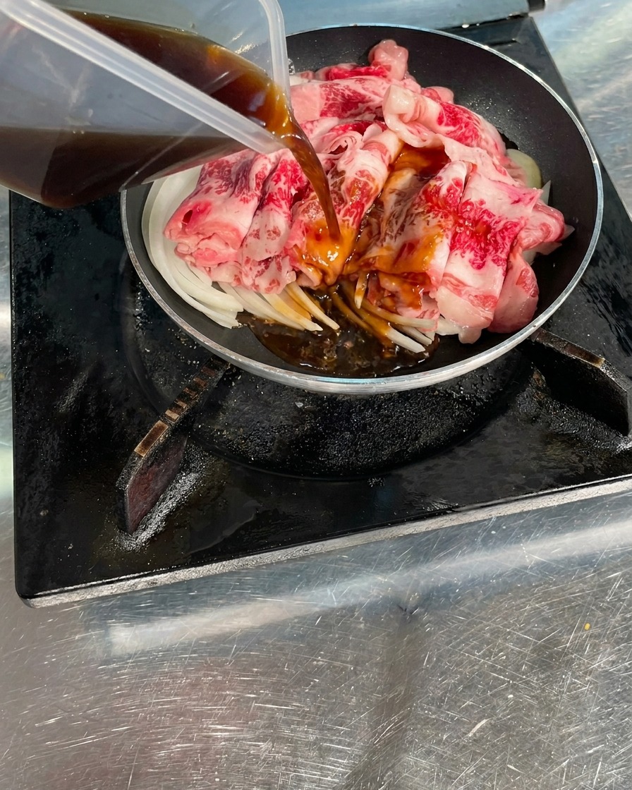 Une sauce savoureuse brun foncé versée depuis un récipient transparent sur des tranches de bœuf cru et des oignons dans une poêle.