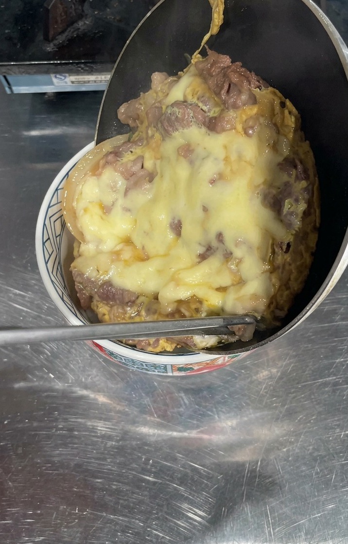 Une poêle inclinée au-dessus dun bol de riz blanc, laissant glisser une épaisse couche de bœuf cuit et de fromage jaune fondu pour recouvrir la surface.