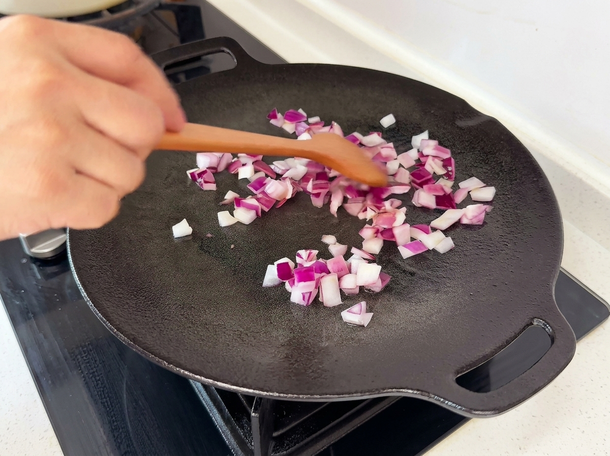 Des dés doignon rouge sautés dans une poêle plate noire à laide dune spatule en bois.