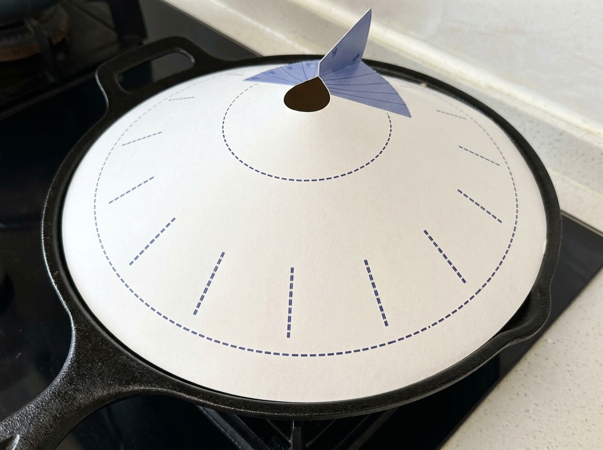 Une poêle en fonte noire recouverte dun couvercle en papier conique blanc avec des motifs bleus, posée sur une plaque de cuisson.
