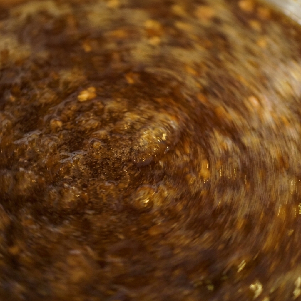 Gros plan dune sauce brun foncé bouillonnant vigoureusement dans une casserole tout en étant remuée rapidement.