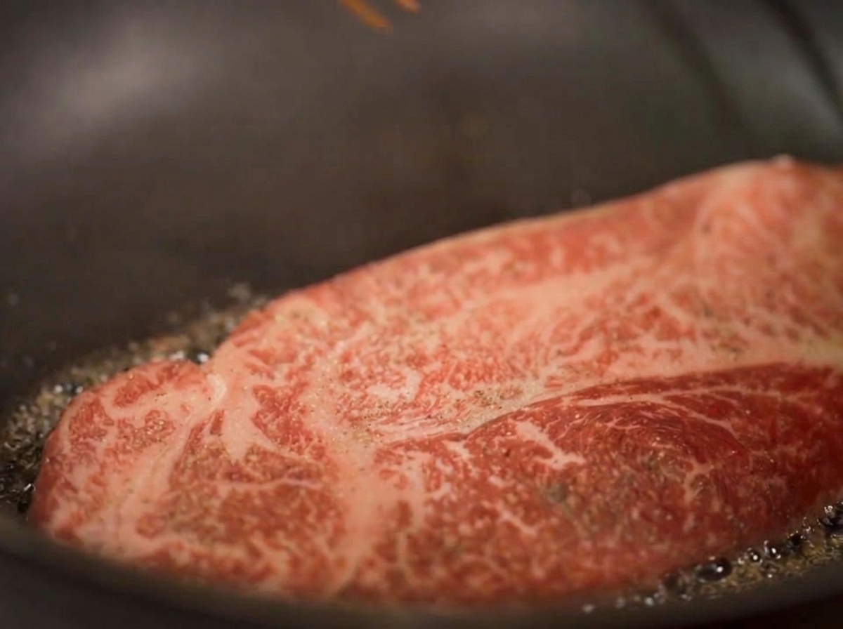 Gros plan dun steak épais saisissant dans lhuile, avec de la vapeur visible qui sélève et les bords inférieurs qui dorent.