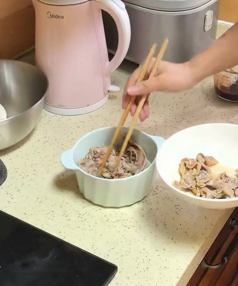 Une personne utilisant des baguettes en bois pour transférer des lamelles de bœuf blanchies dune assiette blanche vers un bol contenant les oignons cuits.