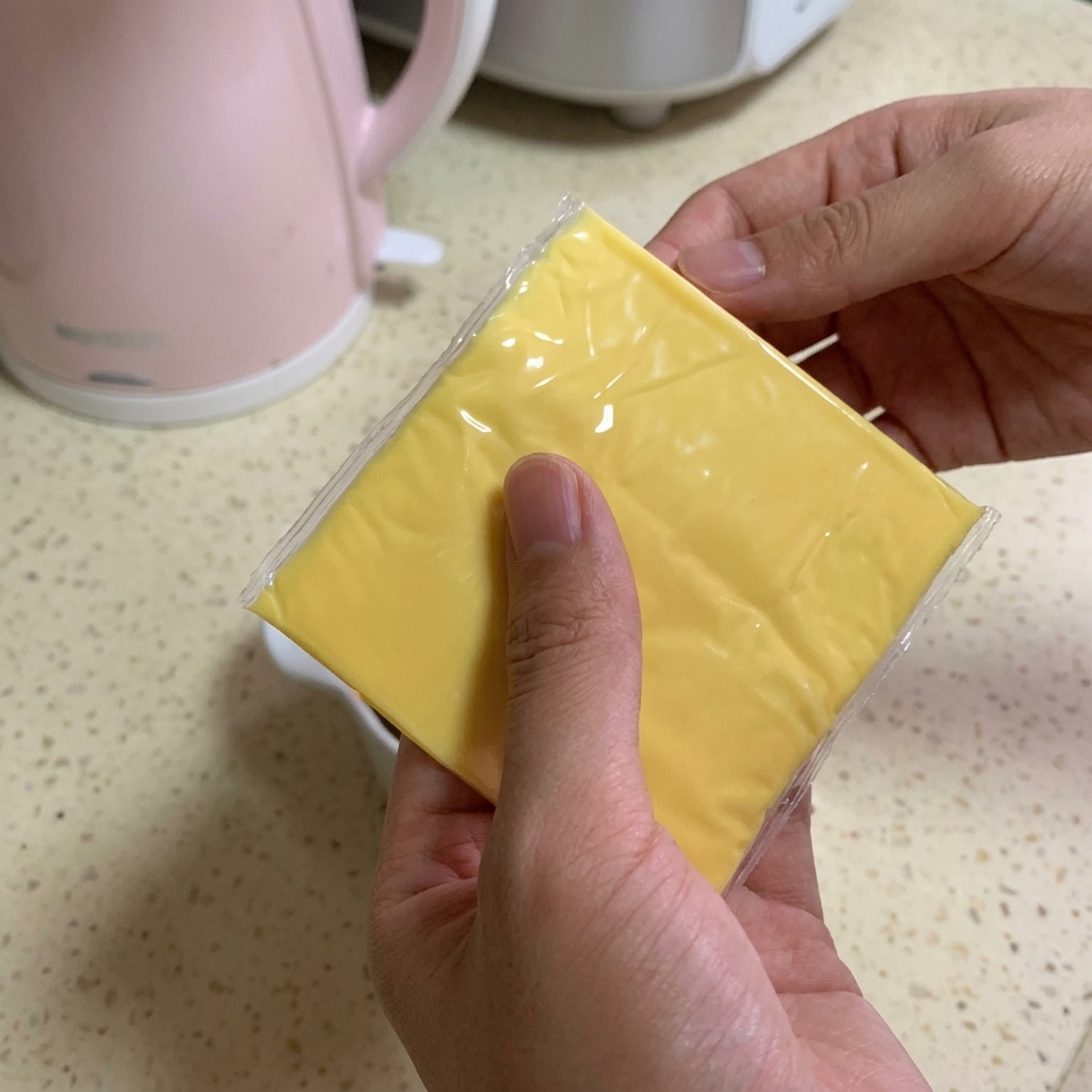 Une personne tenant deux tranches carrées de fromage fondu jaune vif au-dessus dun bol rempli de bœuf et de sauce foncée.