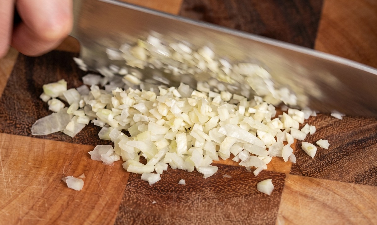 Gros plan dun couteau de chef éminçant finement des gousses dail sur une planche à découper en bois.