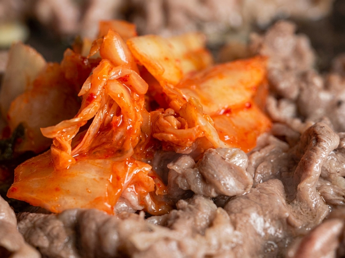 Une généreuse portion de kimchi rouge vif mélangée à de fines lamelles de bœuf dans une poêle à frire.