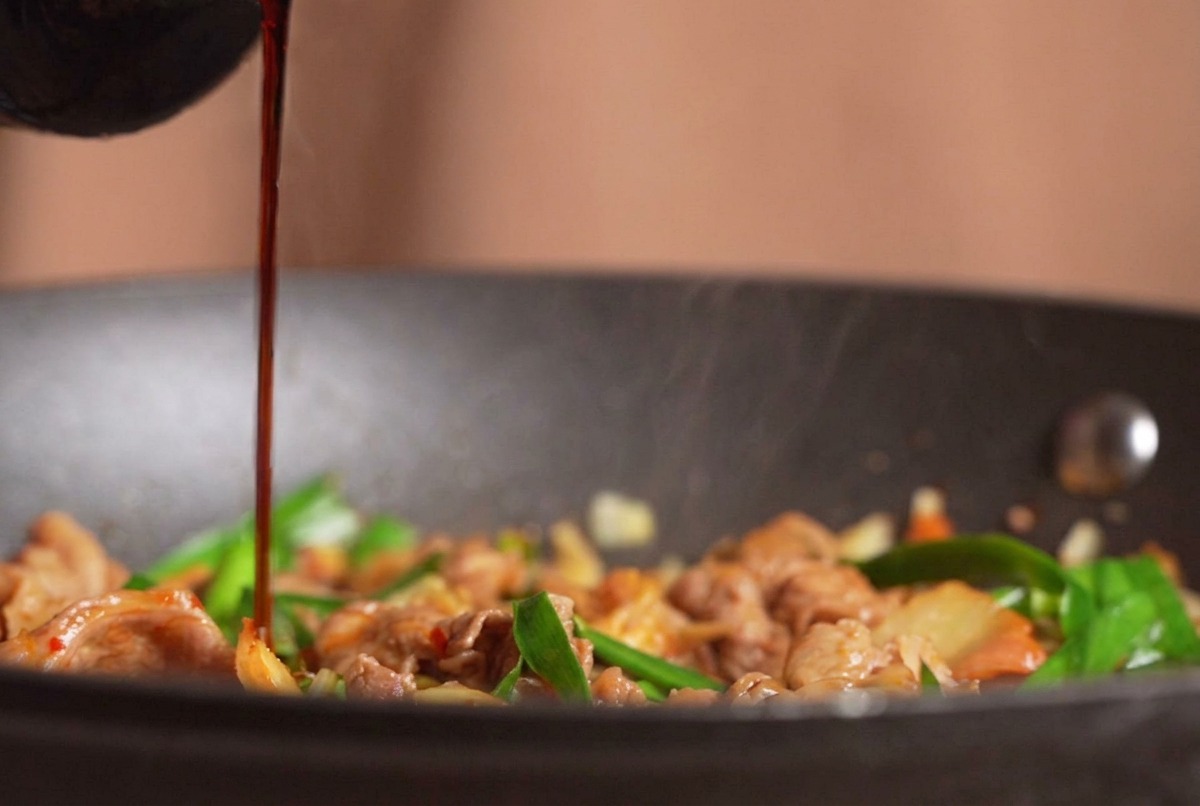 De la sauce soja claire versée depuis une bouteille sur un sauté fumant de bœuf, de kimchi et de ciboulette.