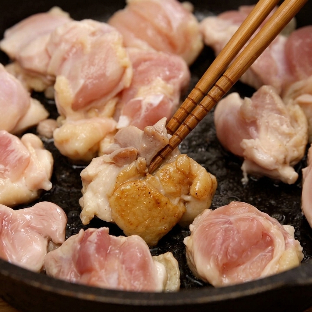 Morceaux de poulet sautés dans une poêle et remués avec des baguettes en bois jusquà légère coloration.