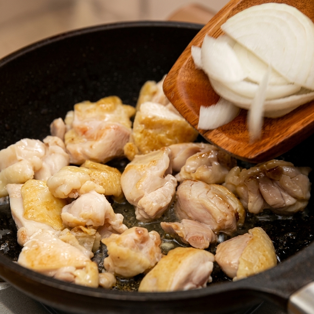 Lamelles doignon blanc ajoutées à laide dune spatule en bois dans la poêle contenant le poulet saisi.